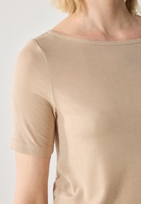 T-shirt beige à côtes avec des manches courtes, dotée d'un col large et d'une texture lisse, mettant en avant une coupe ajustée.
