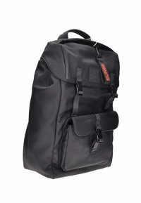Mochila de tela negra con solapa en la parte superior, bolsillo frontal y correas ajustables. Presenta un cierre de clip y un parche con logotipo en la parte delantera.