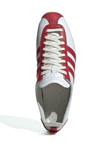 Vita lädersneakers med röda accenter, med rund tå, platta beige snören och tre röda ränder på sidan. Södra insida.