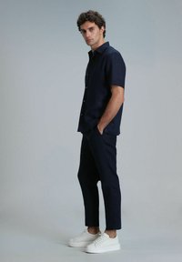 Marineblauw kortom shirt met knopen, gecombineerd met slim-fit marineblauwe broek en witte sneakers. Soepele stof met een casual pasvorm en een minimaal ontwerp.