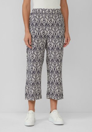 Die bedruckte, knöchellange Hose hat ein Navyblau-und-Creme-Blattmuster, einen elastischen Bund und ein leichtes Material. Kombiniert mit weißen Turnschuhen.