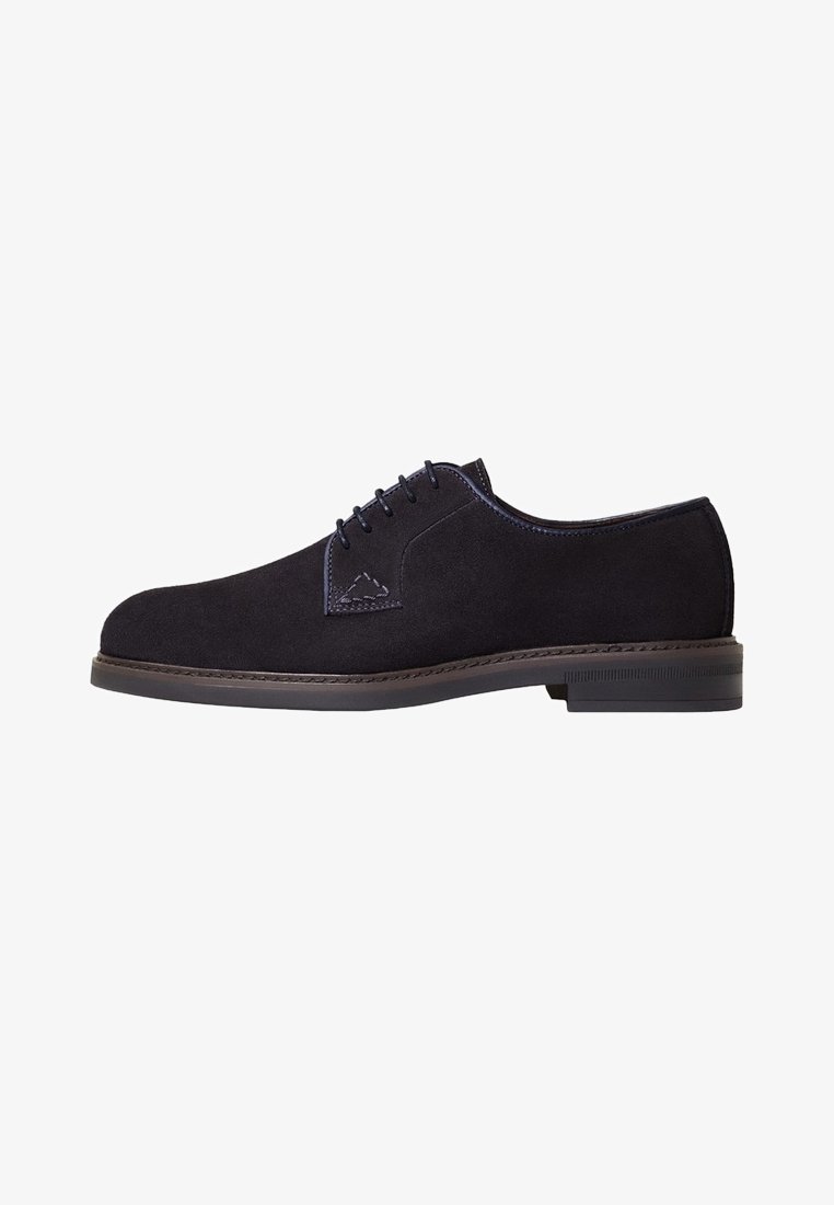 Chaussure oxford en suede noir avec un bout rond, un laçage, des coutures contrastantes et une semelle en caoutchouc plate. Un style facile à porter au quotidien.