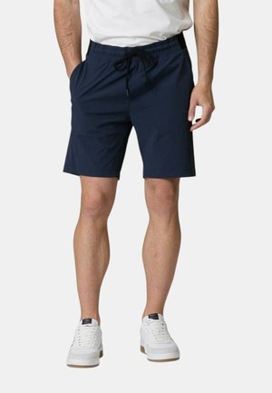 Pantaloni da bagno blu navy con elastico in vita e cordoncino, tasche laterali e tessuto morbido. Abbinati a scarpe da ginnastica bianche.