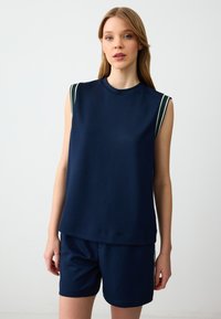 Navyblauwe mouwloze top van zacht materiaal, met witte en groene gestreepte accenten op de schouders; gecombineerd met bijpassende navy shorts.