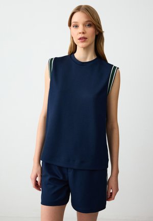 Débardeur sans manches bleu marine en tissu doux, présentant des accents rayés blancs et verts sur les épaules ; associé à un short bleu marine assorti.