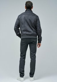 Chaqueta de ante gris con cuello alto, combinada con pantalones ajustados grises. Zapatillas blancas completan el conjunto. Diseño minimalista sin patrones visibles.