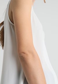 Top bianco senza maniche realizzato in tessuto leggero; texture liscia con una vestibilità comoda, caratterizzato da un colletto rotondo e senza componenti metallici visibili.