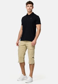 Czarna koszulka polo z krótkim rękawem, khaki szorty cargo i białe sneakersy. Szorty cargo mają kieszenie i cuffs.