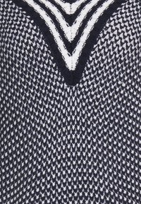 Pull en tricot avec un motif en chevrons bleu marine et blanc, décolleté en V et tissu texturé avec un tissage dense.