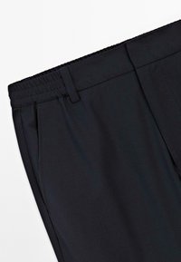 Zwarte broek met een elastische tailleband, voorzien van twee zijzakken en een gladde textuur. Het ontwerp is eenvoudig zonder zichtbare patronen of accenten.