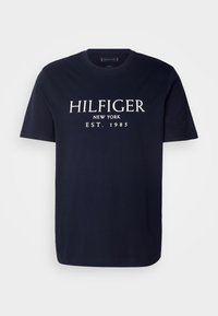 Navy blue cotton T-shirt with short sleeves, featuring white text: "HILFIGER NEW YORK EST. 1985" centered on the front. Classic crew neck design.
