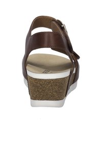 Hnědé kožené sandály na klinu s kotníkovým popruhem, bílou gumovou podrážkou, korkovou mezipodrážkou a hladkým vnitřním povrchem. Navrženo pro pohodlí a oporu.