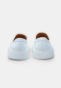 Baltas ādas slip-on apavi ar gludu tekstūru, noapaļotu formu un brūnu iekšējo oderi. Minimālistisks dizains ar smalkiem stikojumiem.