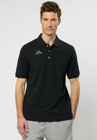 Zwarte poloshirt met korte mouwen, drie knopen bij de kraag en een wit logo aan de linkerkant van de borst. Gladde stof, normale pasvorm.