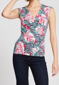 Blomstret ærmeløs top med v-halsdesign, prydet med pink og grønne tropiske blade imod en hvid baggrund. Tætsiddende og blødt materiale.