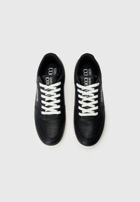 Μαύρα δερμάτινα αθλητικά παπούτσια με λευκές κορδόνες, διάτρητες λεπτομέρειες, λεία υφή και αντίθετη λευκή σόλα. Ορατό λογότυπο στο εσωτερικό.