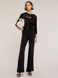 Czarna satynowa bluzka z rękawami o długości trzech czwartych, czarne spodnie z wysokim stanem i rozszerzanymi nogawkami, matowy czarny pasek, kremowa torebka oraz geometryczny naszyjnik w odcieniach różu.