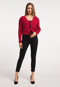 Röd stickad cardigan med spetsdetaljer och knytning fram, kombinerad med svarta högmidjade skinny jeans och svarta spetsiga klackskor.