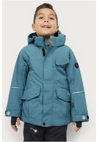 Teal vandtæt jakke med hætte, flere frontlommer, reflekterende striber og sorte detaljer. Har en frontlynlås og velcro-lukninger.