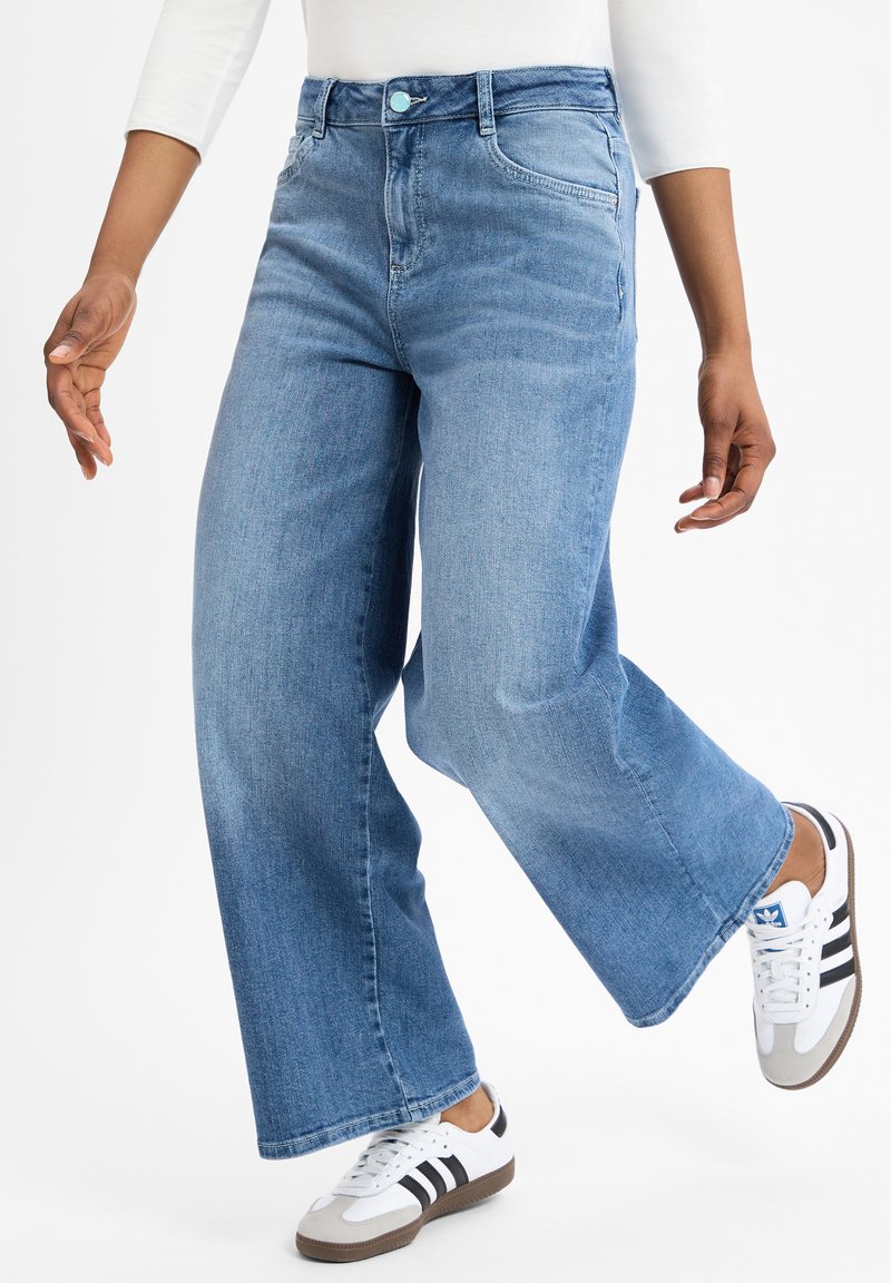 Lichtblauwe wijde jeans met een hoge taille en subtiele vervaagde textuur, gecombineerd met wit en zwart gestreepte sportschoenen.