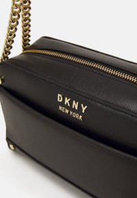 Czarna skórzana torebka o fakturowanej powierzchni, złote okucia, zamek błyskawiczny i łańcuszkowy uchwyt. Na przedniej stronie znajduje się tłoczony napis „DKNY NEW YORK”.