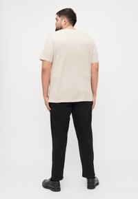 Beige t-shirt met korte mouwen en een ronde hals, gecombineerd met zwarte broeken, getoond vanaf de achterkant. Gladde textuur, casual pasvorm.