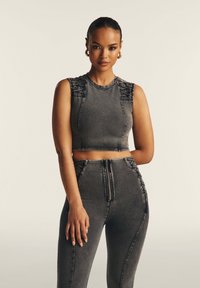 Top corto in denim grigio con accenti testurizzati sulle spalle, abbinato a pantaloni in denim grigio a vita alta con zip frontale e dettagli laterali.