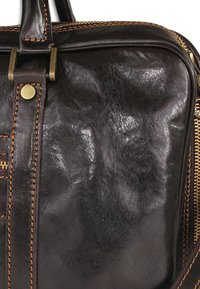 Brown leather bag with a glossy finish, reinforced stitching in tan, brass hardware, and a zip closure along the top edge.