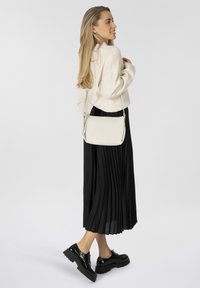 Bolso cruzado blanco hecho de material suave, diseño rectangular con un perfil delgado, combinado con una falda negra con pliegues y zapatos negros brillantes.