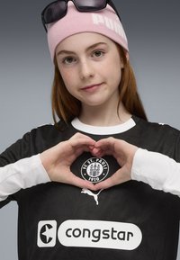 Sort trøje med hvide accenter og et logo af FC St. Pauli. Lyserød hue med "PUMA." Hænder der danner en hjerteform over logoet.