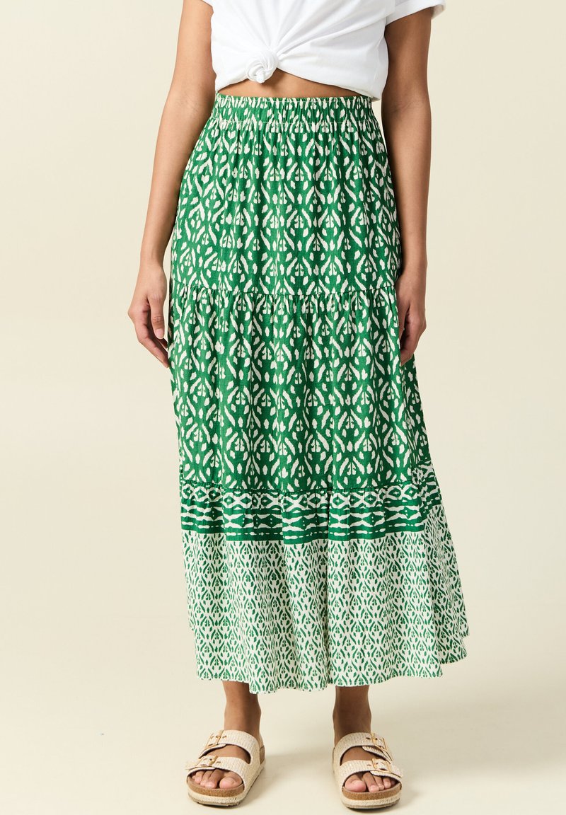 Groene maxi-rok met patroon en elastische tailleband; heeft een gelaagd ontwerp met witte geometrische motieven en een contrasterende onderband.