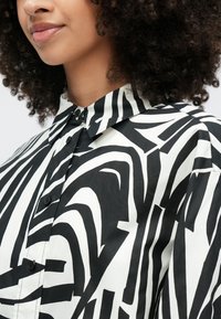 Πουκάμισο με ασπρόμαυρο μοτίβο, με έντονες, αφηρημένες ρίγες, κλασικό γιακά και κουμπιά μπροστά, κατασκευασμένο από λείο ύφασμα.