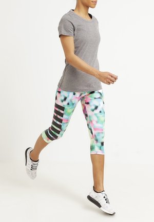 Personne marchant avec une chemise à manches courtes grise, des leggings capri multicolores avec des rayures noires, et des chaussures de sport blanches avec des semelles noires.