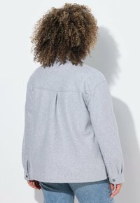 Grijze wolmixjas met een ontspannen pasvorm, knoopmanchetten, rugplooi-detail en een gladde textuur, gedragen met lichtblauwe jeans.