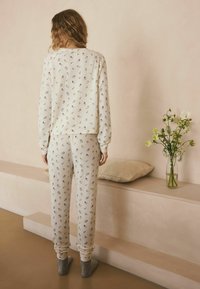 Schlafanzug-Set in Cremefarben mit gerippter Struktur, Blumenmuster in gedämpften Farben, mit langen Ärmeln und bundgefederten Hosen.