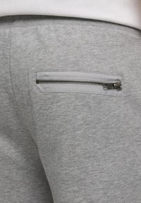 Primer plano de tela de pantalones deportivos grises con un bolsillo horizontal con cremallera metálica en la parte trasera.