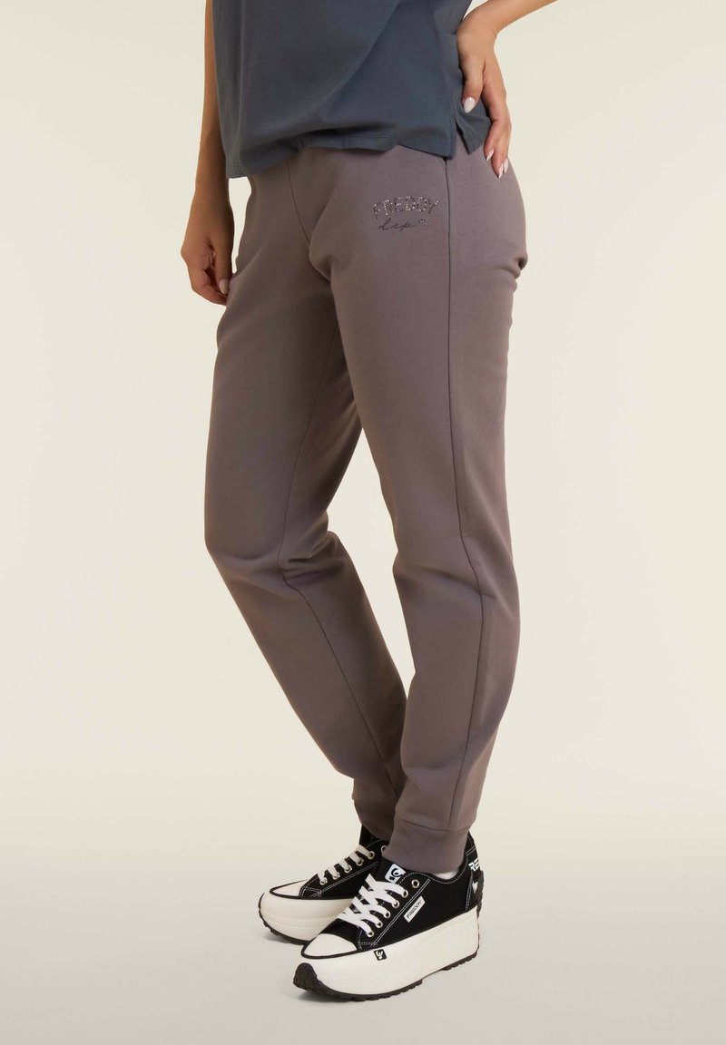 Pantalones deportivos gris claro con un diseño ajustado, que presentan un pequeño logo como detalle y puños acanalados, combinados con zapatillas negras de plataforma.