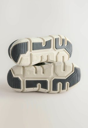 Sport shoes with a textured white and gray sole. Features deep grooves and patterns for traction. Bottom view highlights construction details.