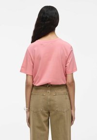 T-shirt in cotone rosa con maniche corte e scollatura rotonda, indossato con pantaloni beige a vita alta dotati di due tasche posteriori.