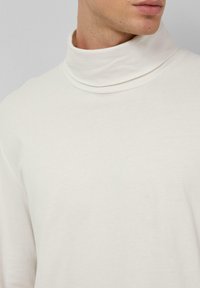 Sweter polo w kolorze kremowym, z miękkiego materiału, luźny krój, lekko układany kołnierz, długie rękawy z minimalnymi detalami szycia.
