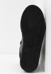 Svart såle med teksturert overflate og avrundede kanter; glatte sider i en mørkere nyanse; minimalistisk design uten synlig merkevare.