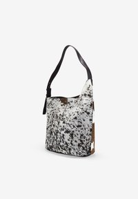 Bolso de hombro hecho de piel de vaca moteada, con una textura suave, forma asimétrica y una correa de cuero negro para llevar.