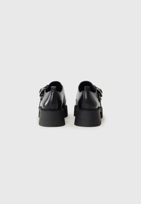 Scarpe in pelle nera con suola in gomma spessa, caratterizzate da una finitura liscia e cuciture visibili. Progettate con tacco rialzato e dettaglio a fibbia.