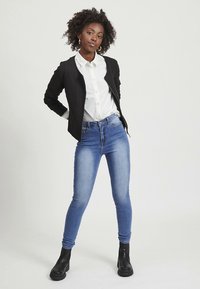 Black textured blazer over a white button-up shirt, paired with light blue skinny jeans and black ankle boots. White background.