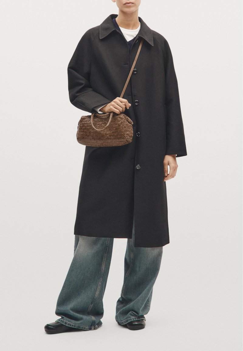 Sort, kravet overtøj med lige snit og knaplukning, parret med brede jeans og en lille, vævet brun håndtaske.