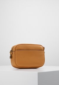 Torba ze skóry w kolorze jasnobrązowym o prostokątnym kształcie, teksturowanej powierzchni, kontrastowym przeszyciu oraz małym metalowym akcentem na zamku.