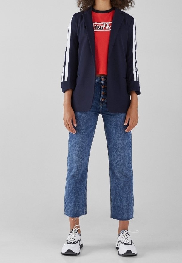 Mörkblå kavaj med vita ränder, röd t-shirt med grafik, högmidjade blåjeans och svart- och vit-sneakers. Avslappnad lager-på-lager-outfit.