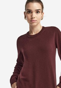 Burgunderfarbener Pullover mit Rundhalsausschnitt, gerippten Bündchen und weichem Material, ausgestattet mit langen Ärmeln und einem schmalen Schnitt.