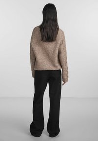 Beige knitted sweater with textured pattern and cable-knit sleeves, paired with black wide-leg pants.