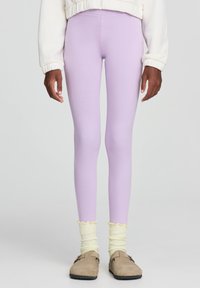 Leggings lilla con una texture liscia, vita alta e design aderente. Abbinati a calzini gialli a volant e scarpe slip-on color beige.